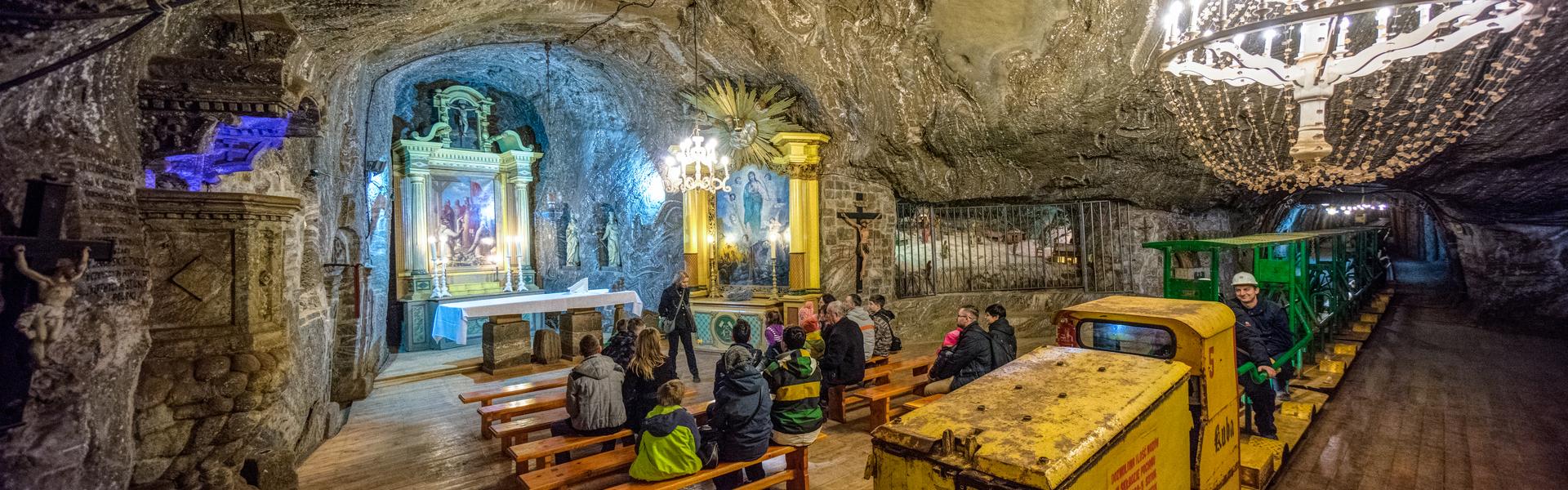Kaplica świętej Kingi, turyści słuchający opowieści przewodnika oraz podziemna kolejka w Kopalni soli w Bochni
