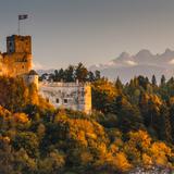 Średniowieczna twierdza - zamek położony na wzgórzu, pośród drzew w jesiennych barwach, w tle góry.