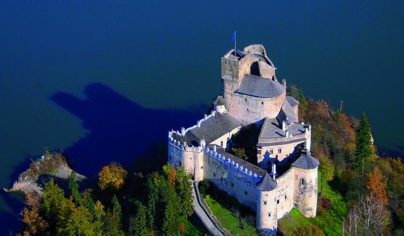 Średniowieczny zamek - twierdza położony pośród drzew nad brzegiem jeziora, w którym odbija się jego cień. Widok z lotu ptaka.