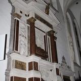 Jasny nagrobek w ścianie z ciemnymi kolumnami i tablicami oraz z dwiema rzeźbami, jedna nad drugą.