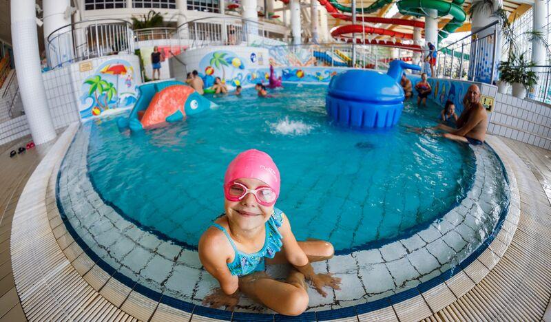 Dziewczynka w czepku i okularach pływackich przy brzegu basenu