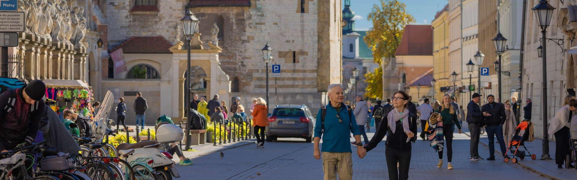 Kobietę i mężczyznę, trzymających się za ręce, spacerujących po ulicy. Po lewej i prawej zabudowania.