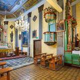 Wnętrze drewnianego kościoła z kolorowymi polichromiami, ołtarzem, amboną i ławami.