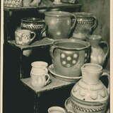Wzorzysta ceramika ze zbiorów muzealnych na archiwalnym zdjęciu stojąca na schodach. Ceramika składa się z wazonów, kubków i garnczków.