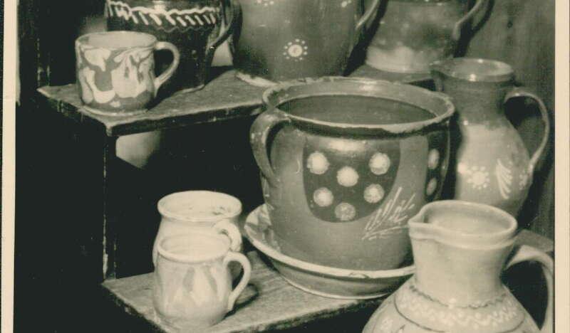 Wzorzysta ceramika ze zbiorów muzealnych na archiwalnym zdjęciu stojąca na schodach. Ceramika składa się z wazonów, kubków i garnczków.