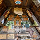 Drewniana ściana z kilkunastoma drewnianymi tablicami oraz obrazem Matki Boskiej.