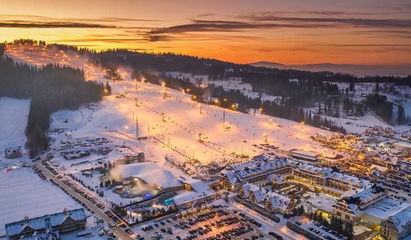 Zdjęcie z drona przedstawiające Hotel Bania na tle ośnieżonego stoku narciarskiego.