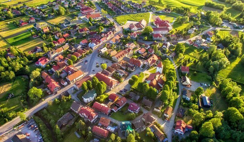 Panorama Lipnicy Murowanej z drona. Widać duży rynek, odchodzące od niego uliczki i ulice obwodowe tworzące owalnicę, ładne domy, dużo zieleni.