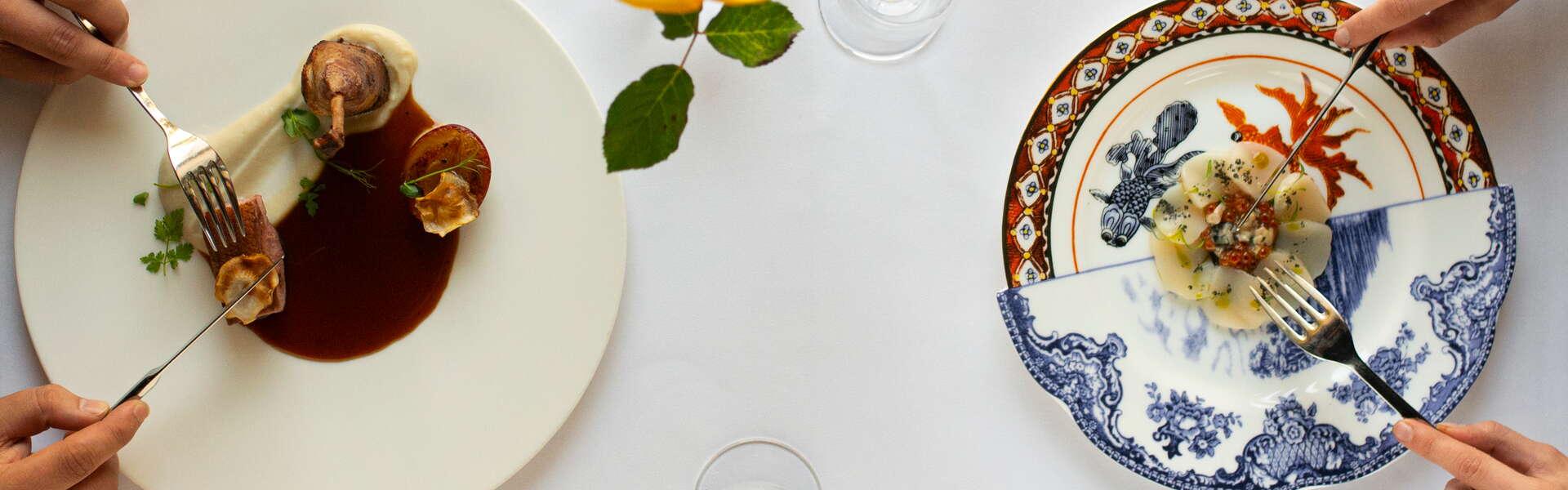 2 Teller mit Gerichten, elegant serviert, weiße Tischdecke und Weingläser