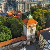 Widok z drona na Bramę Floriańską oraz pozostałą część murów obronnych w Krakowie. Za murami korony drzew, a na dalszym planie barbakan oraz kamienice.
