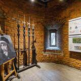 Fragment sali w ceglanej wieży z małym oknem w Murach obronnych w Krakowie, gdzie znajdują się informacje na temat miejsca, obraz i kilka sztuk broni.