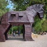 Zrobiony z drewna duży koń z drabiną po której można do niego wejść i dwoma okienkami - przez jedno z nich wygląda dziecko w Parku Mitologii Zatorland